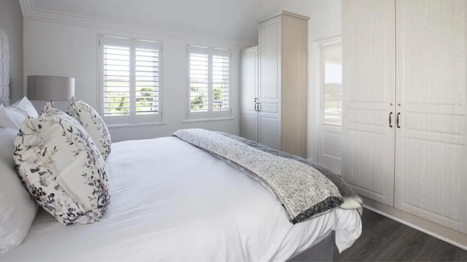 Elegantly styled double bedroom with floral cushions and plantation shuttered windows at Winelands Golf Lodges at De Zalze, Stellenbosch